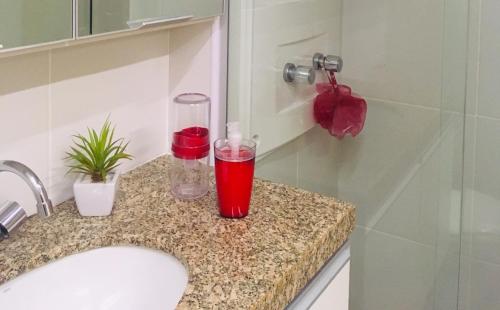 La salle de bains est pourvue d'un lavabo avec un comptoir en verre rouge. dans l'établissement Apartamento na Ponta Verde Maceió Facilities, à Maceió
