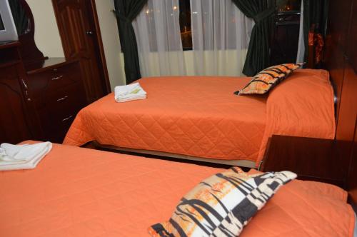 two beds in a room with orange sheets at Balcones del Río Hotel in Latacunga