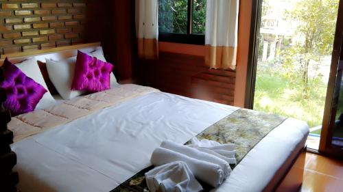 a bedroom with a bed with purple pillows and a window at Khai Mook Homestay in Nan