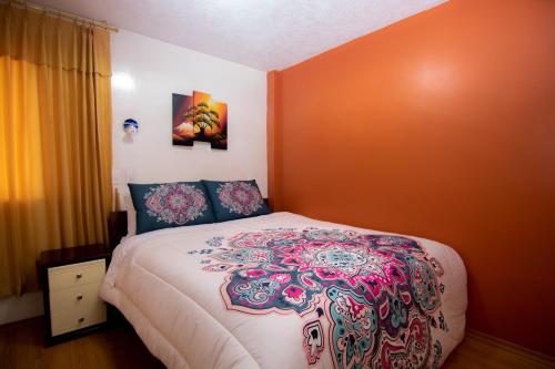 a bedroom with a bed with an orange wall at Hostal Alpachaca - New Quito Airport in Tababela