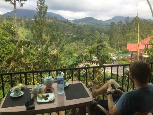 a man sitting at a table on a balcony with a view at Princess of Dickoya Homestay in Hatton