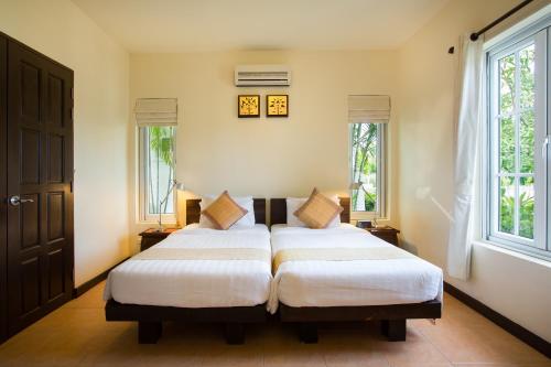 two beds in a room with two windows at Villa Bougainvillea in Hua Hin