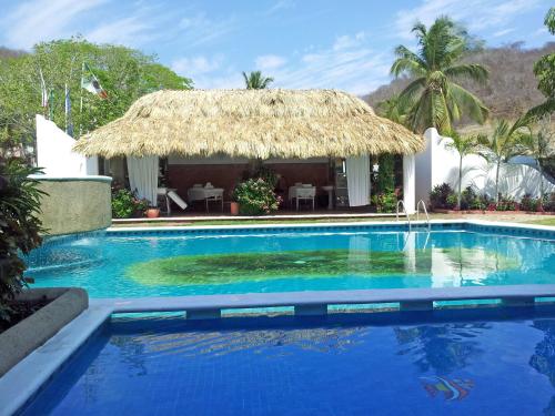 a resort with a large blue swimming pool with a thatch roof at Canadian Resort Huatulco in Santa Cruz Huatulco