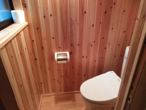 a bathroom with a toilet and a wooden wall at Minpaku Sarai Nikkoya in Okkia