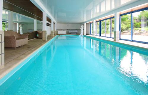 a large swimming pool with blue water in a building at Le Manoir de la mantille in Caudry