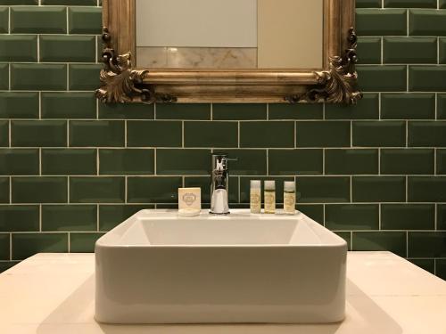 a white sink in a green bathroom with a mirror at Oryza Guest House& Suites in Coimbra