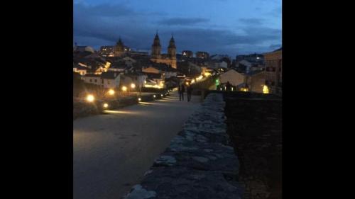 a city at night with people walking down a sidewalk at Lucus Bed in Lugo