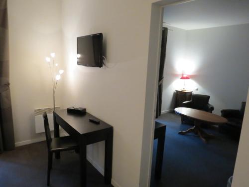 Zimmer mit einem Tisch und einem TV an der Wand in der Unterkunft Hostellerie Du Royal Lieu in Compiègne
