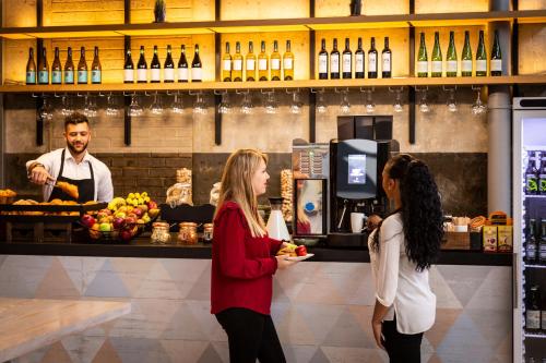 two women standing in front of a bar with a bartender at Aparthotel Adagio London Brentford in Brentford