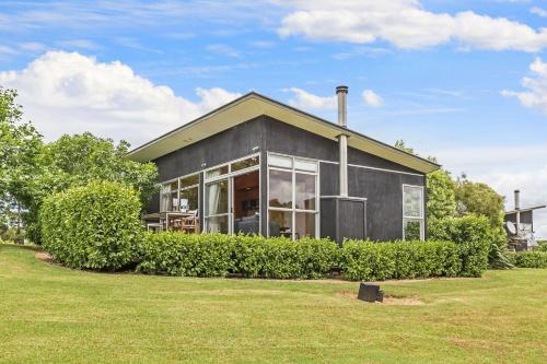 a gray house with large windows and bushes at Riverside Matakana in Matakana