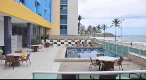 un complejo con piscina, mesas y sillas y la playa en Bahia Flat Apt 124 Farol da Barra, en Salvador