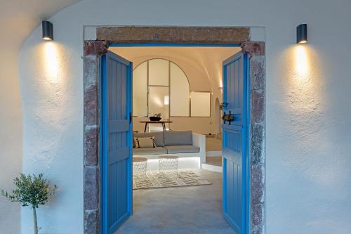 una porta blu aperta che conduce a un soggiorno con divano di Alluvial Santorini Suites a Mesariá