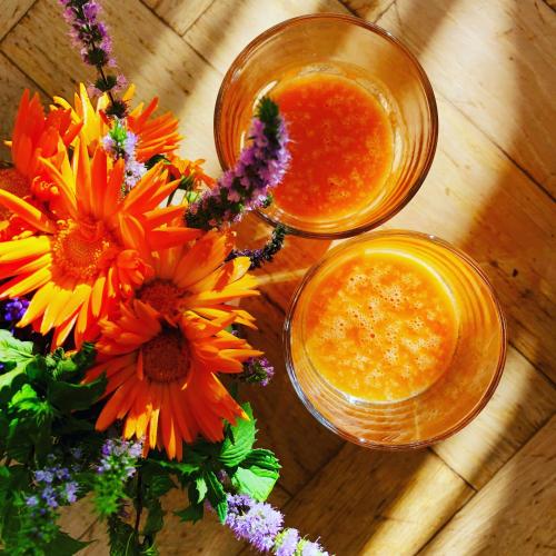 two glasses of orange juice and flowers on a wooden table at Tastecelebration Residence in Andrarum-Brosarp