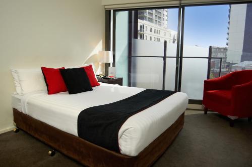 1 dormitorio con 1 cama grande y 1 silla roja en City Edge on Elizabeth Apartment Hotel, en Melbourne
