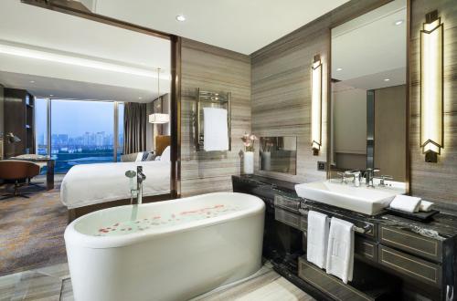 a bathroom with a tub and a sink and a bed at Grand Millennium Shanghai HongQiao in Shanghai