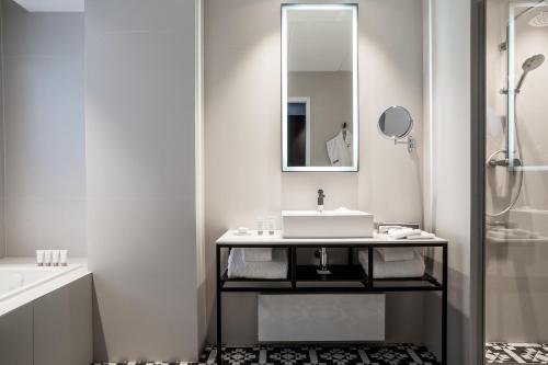 a white bathroom with a sink and a mirror at Hôtel Louvre-Lens - Esprit de France in Lens
