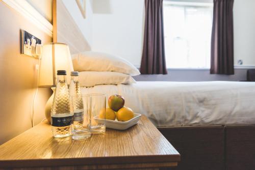 a table with bottles and a bowl of fruit on a bed at The Queensgate Hotel in Peterborough