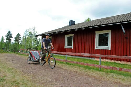 a man riding a bike next to a red building at STF Orsa Hostel in Orsa