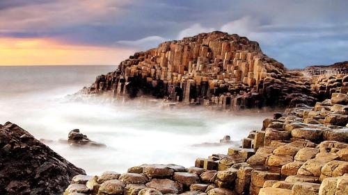 a large rock formation in the ocean with the sun setting at Carnately Lodge in Ballycastle