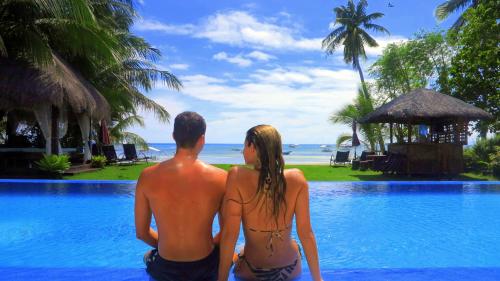 a man and woman sitting on the edge of a swimming pool at Bohol South Beach Hotel in Panglao