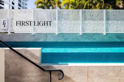 a swimming pool with a sign that reads first light at First Light Mooloolaba, an Ascend Collection Hotel in Mooloolaba