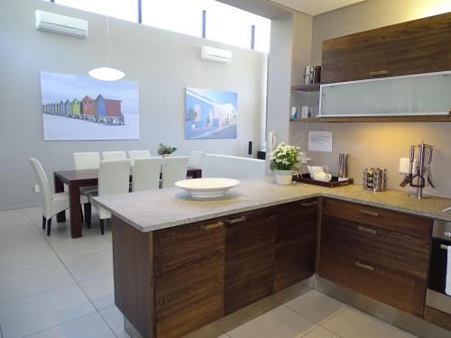 uma cozinha com armários de madeira e uma mesa com cadeiras brancas em Chapman's Peak Penthouse em Hout Bay