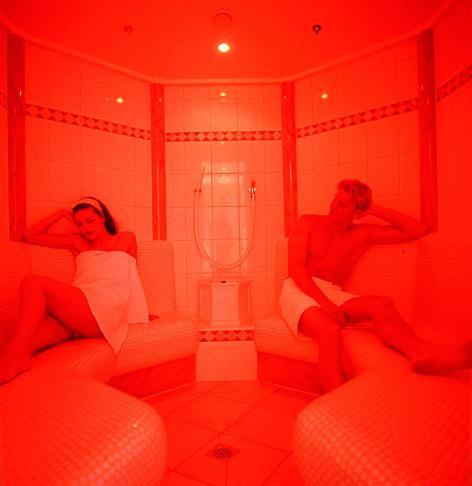 a man and woman sitting in a bathroom with red lights at Sporthotel Krone in Schoppernau