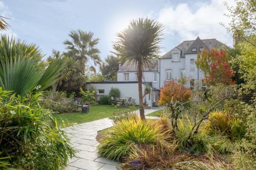 a large white house with palm trees and plants at Hôtel Traiteur Les Ormes, The Originals Relais in Barneville-Carteret