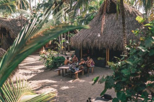 a group of people sitting on benches in front of a hut at Los Hermanos Beach Hostal in Guachaca