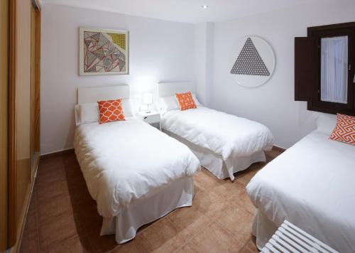 グラナダにあるApartamento Santiagoのベッド3台(白いシーツ、オレンジの枕付)が備わる客室です。