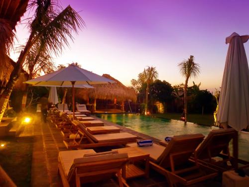 a swimming pool with lounge chairs and an umbrella at Flower Bud Bungalow Balangan in Jimbaran