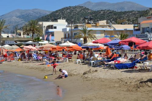 a group of people on a beach with umbrellas at 4S Beach Superior Apartments in Stalida