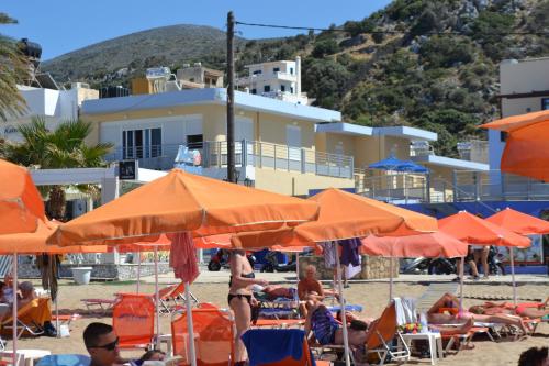 a group of people sitting under orange umbrellas on the beach at 4S Beach Superior Apartments in Stalida