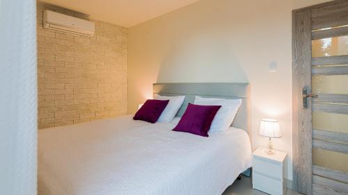 a bedroom with a white bed with two purple pillows at Aparthotel Koroni Home in Raszyn