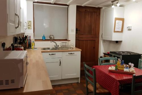 a kitchen with white cabinets and a table with a red table cloth at Dove Cottage, Tideswell in Tideswell