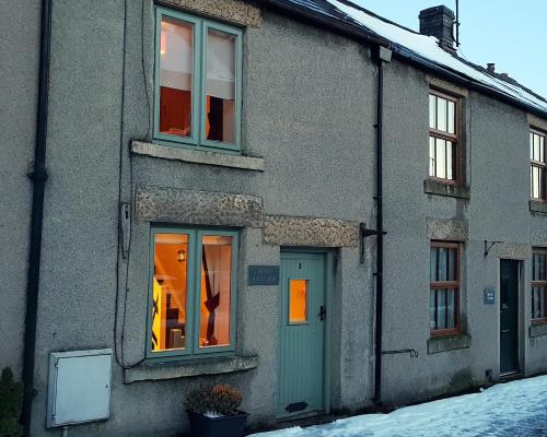 a gray house with a green door and windows at Dove Cottage, Tideswell in Tideswell