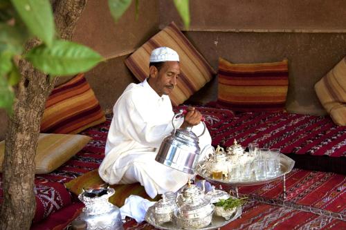 a man sitting on a bed with a tea kettle at Jnane Leila in Marrakech