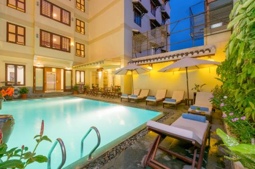 a swimming pool with chairs and umbrellas next to a building at Kiman Hoi An Hotel in Hoi An