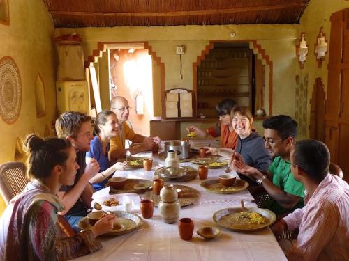 un grupo de personas sentadas alrededor de una mesa comiendo comida en Apani Dhani Eco-Lodge, en Nawalgarh