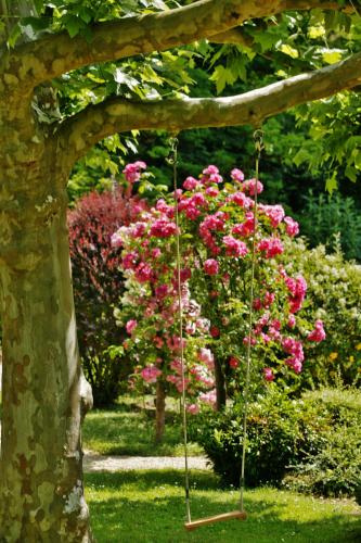 a swing in a garden with pink roses at Les Glycines - Hôtel & Spa - Teritoria in Les Eyzies-de-Tayac