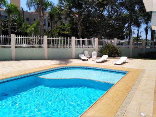 une piscine avec deux chaises longues et une clôture dans l'établissement Brava Apart Hotel, à Florianópolis