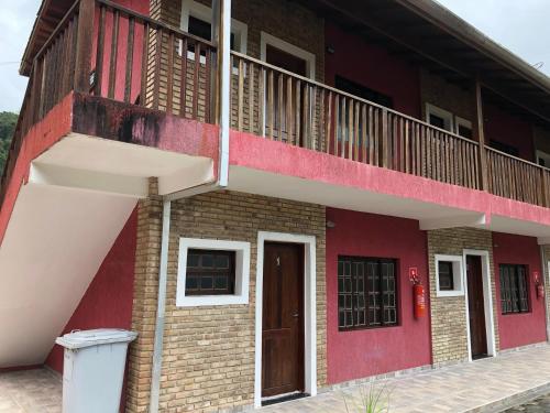 a red building with a balcony and a door at Chalés Buriti in Caraguatatuba