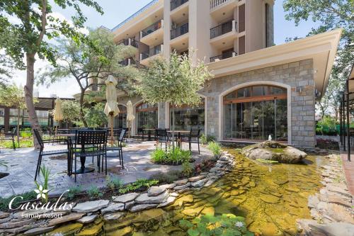 a hotel with a patio with tables and chairs and a pond at Cascadas Family Resort in Sunny Beach