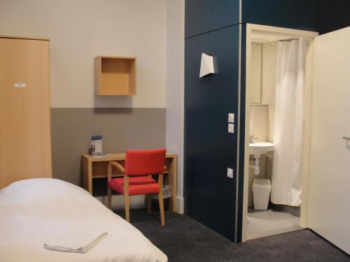 ヌヴェールにあるEspace Bernadette Soubirous Neversのベッド、デスク、赤い椅子が備わる客室です。