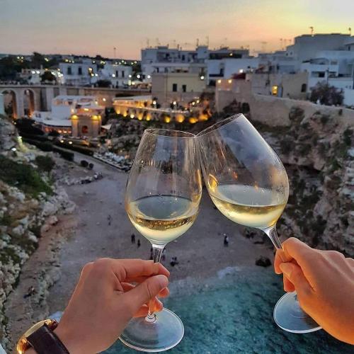 two people holding glasses of white wine overlooking a city at Aquamarea in Polignano a Mare