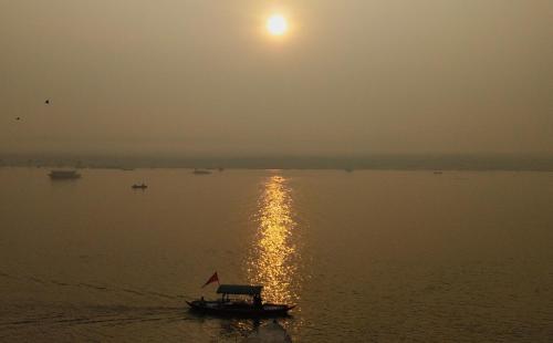a boat on the water with the sun in the sky at Dwivedi Hotels Palace On Steps in Varanasi