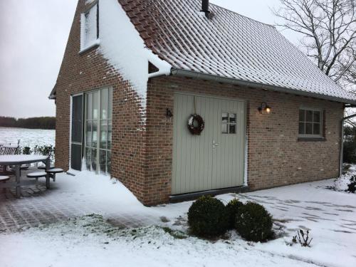 a brick house with a white door in the snow at 't Ligt ter Velde, oase van rust, sauna, directie Brugge in Lichtervelde