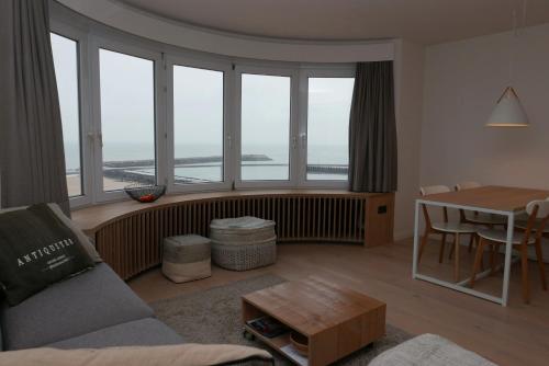 uma sala de estar com um sofá, uma mesa e janelas em Appartement met Zeezicht em Oostende