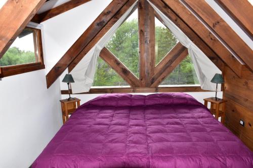 1 dormitorio con cama morada y ventana grande en Andyna - Cabaña frente al río en Trevelín