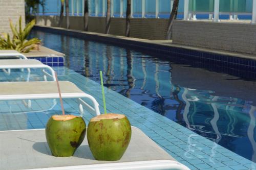 two green fruits sitting on the edge of a swimming pool at Sun Paradise - JTR in Maceió